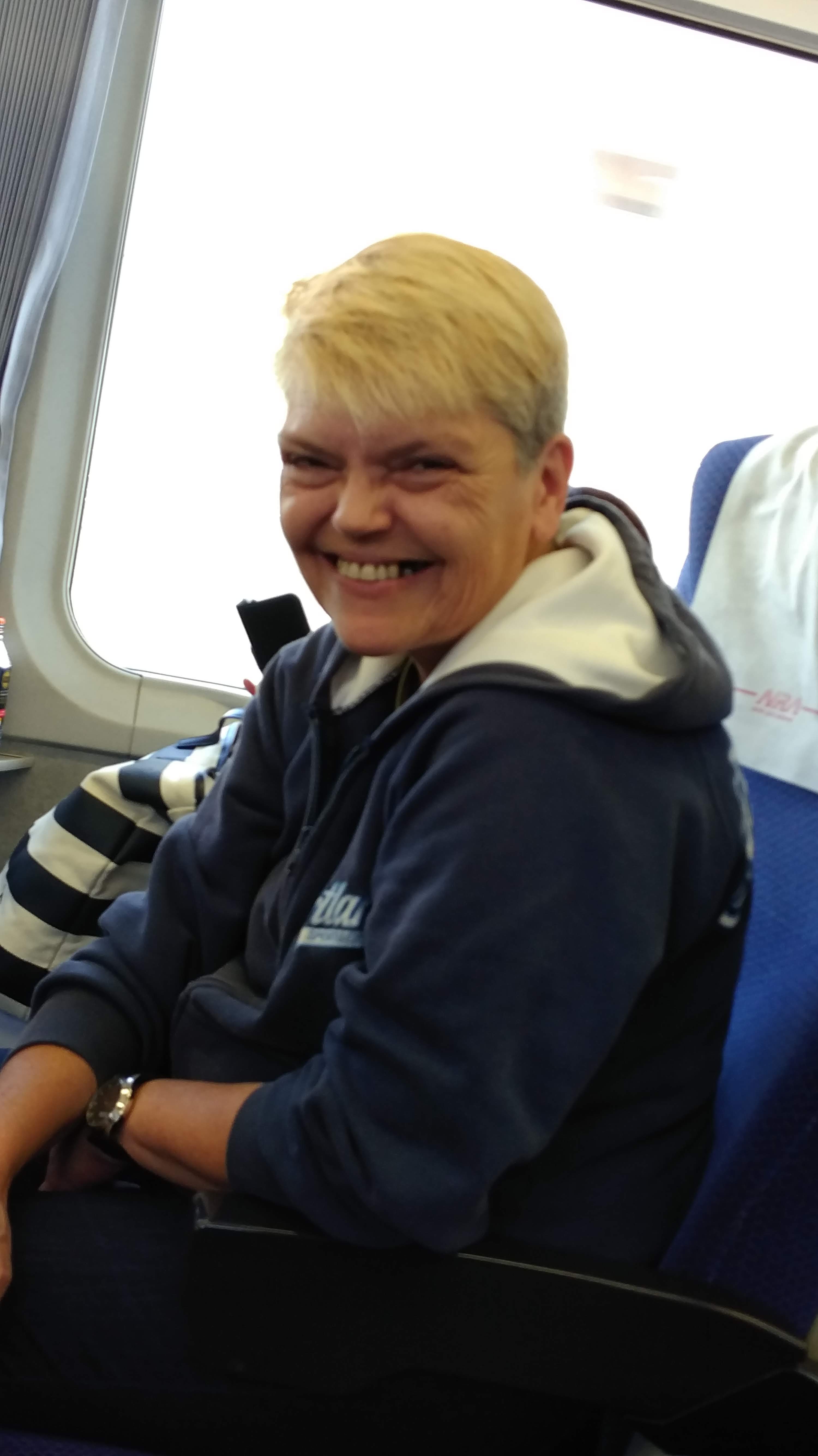 A blonde woman wearing a navy blue hoodie smiles in her seat