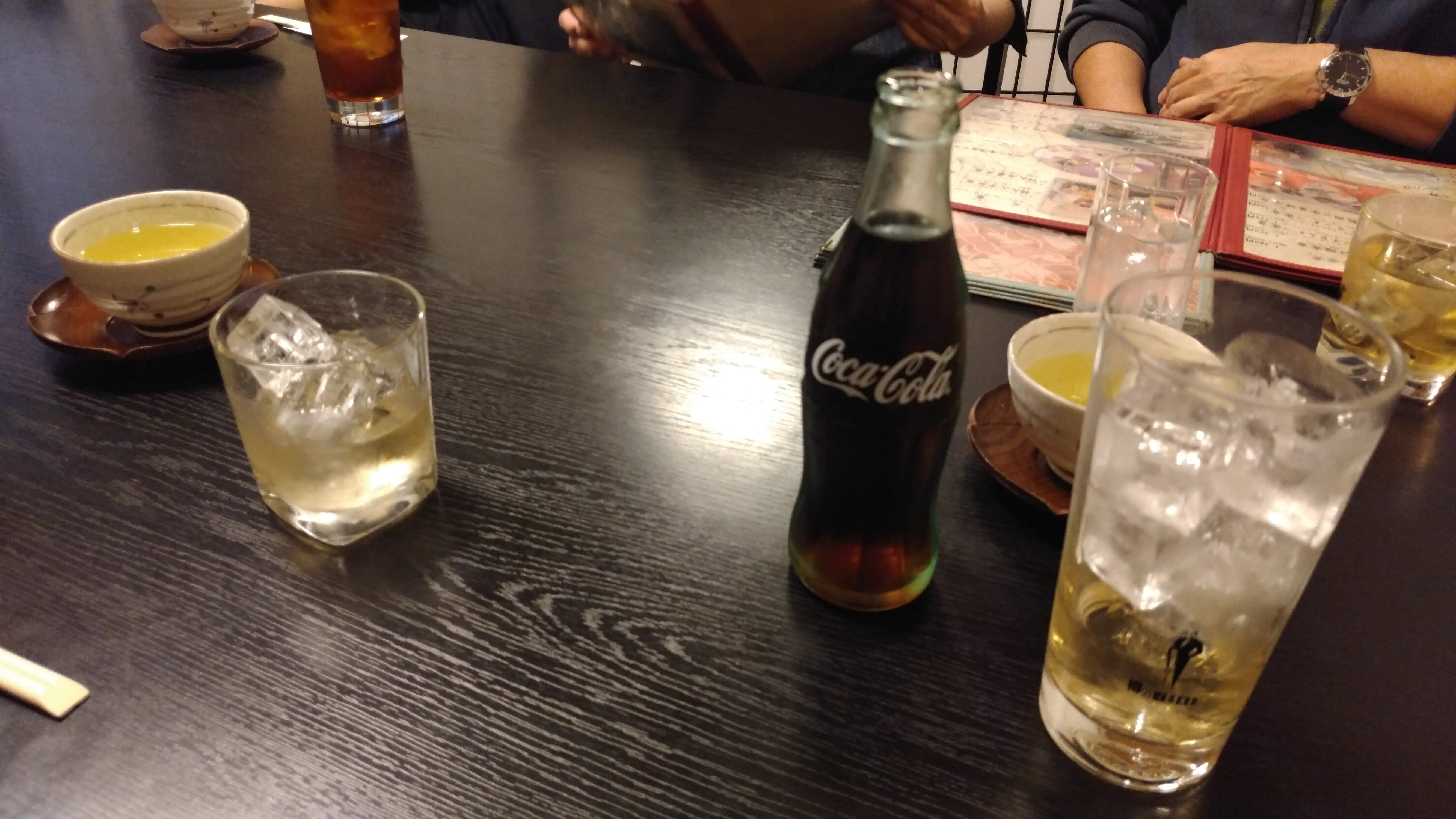 a tall glass, almost half full of spirits next to a glass bottle of coca cola
