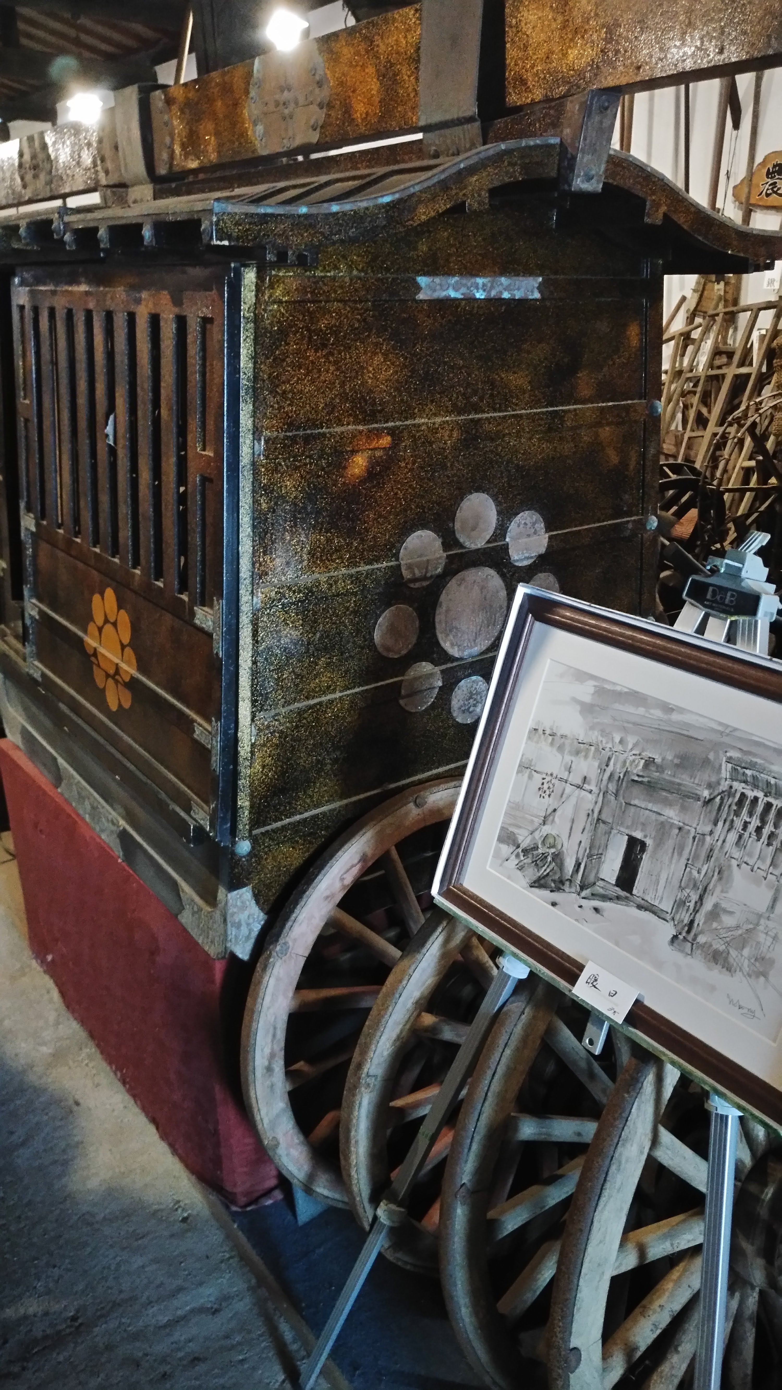 a wooden cart with wooden wheels leaning against it next to a framed black and white painting on a stand