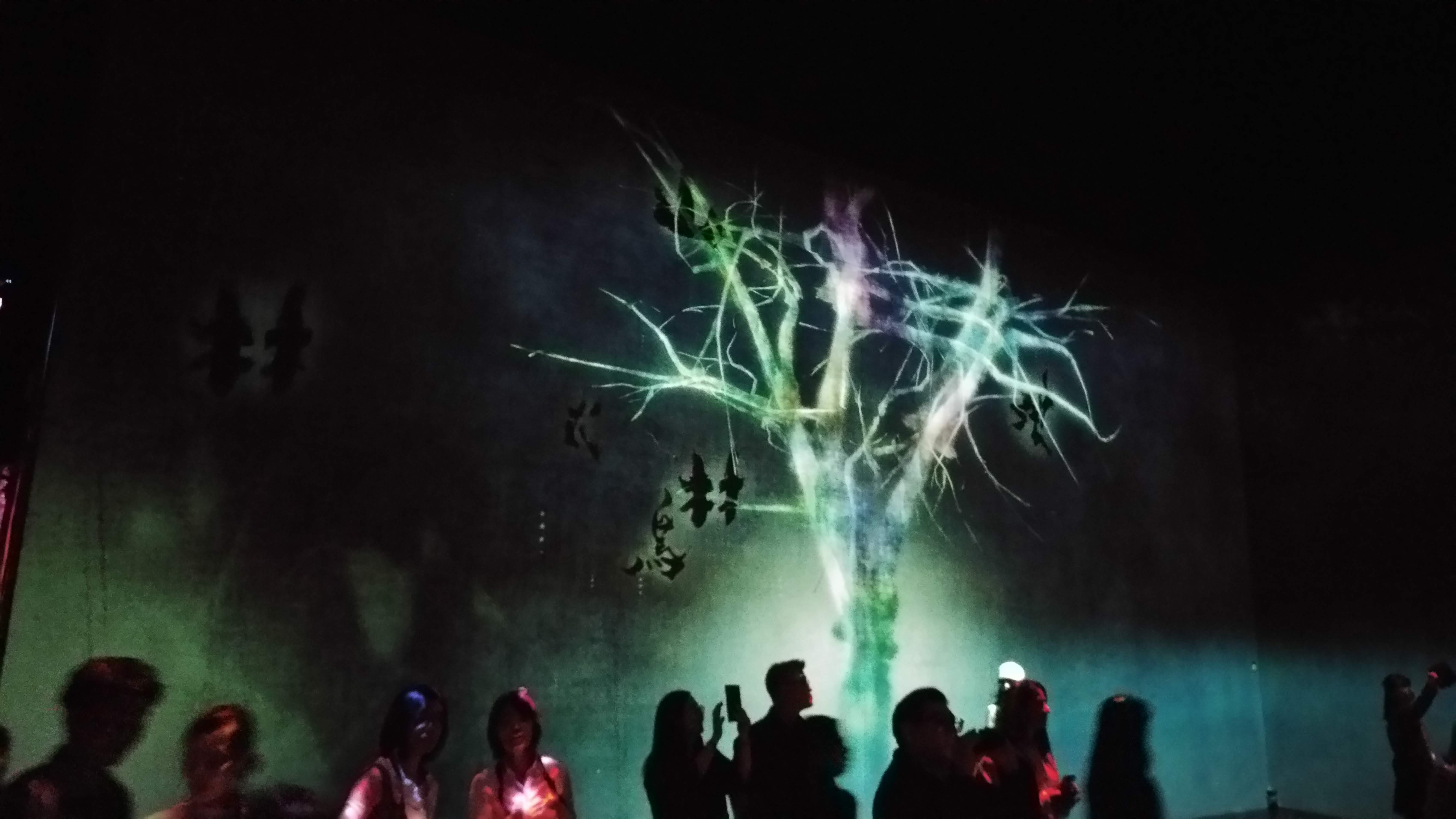 people view a multicoloured tree projected on a wall