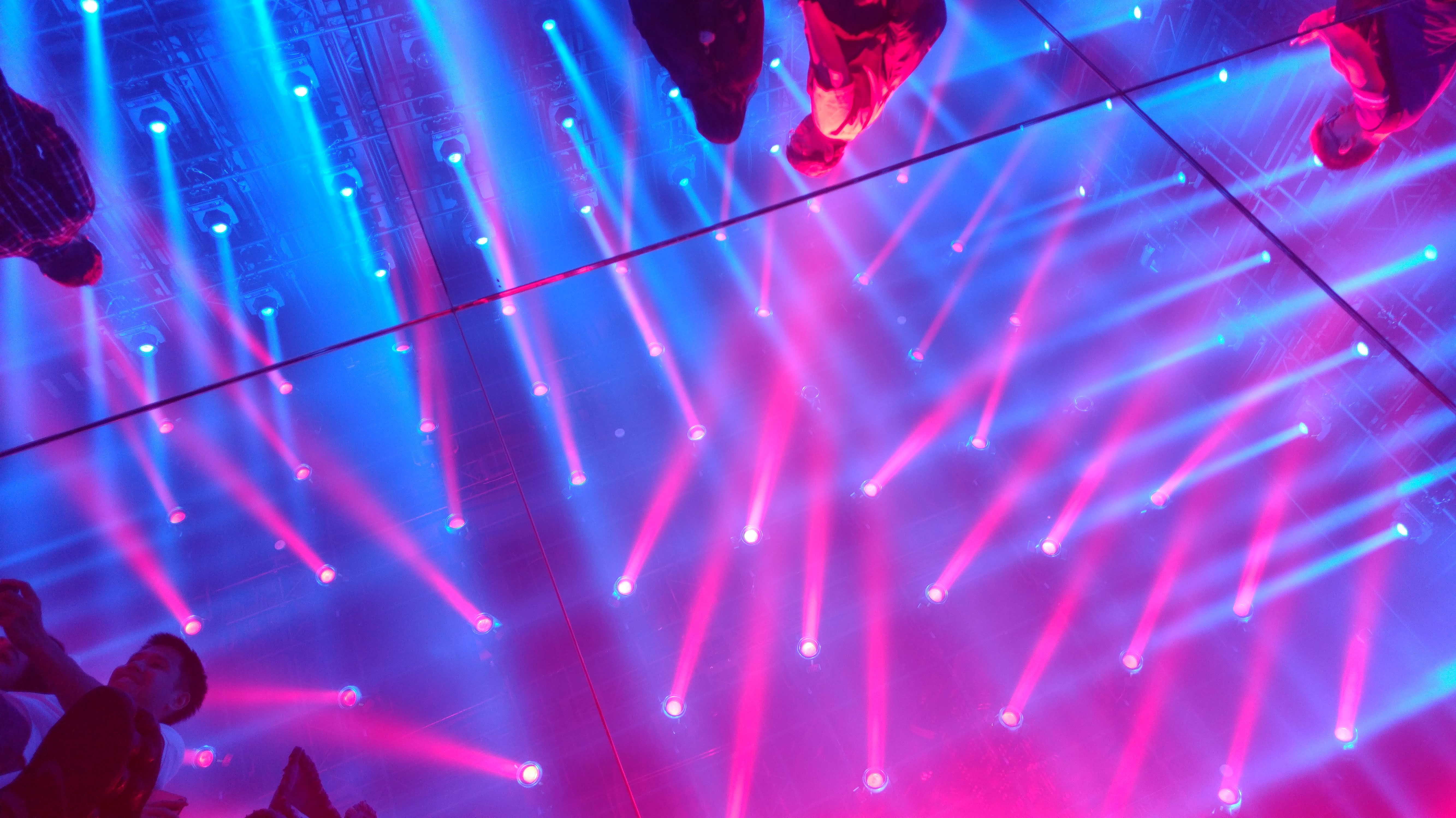 people reflected in a mirrored floor with blue and magenta light beams