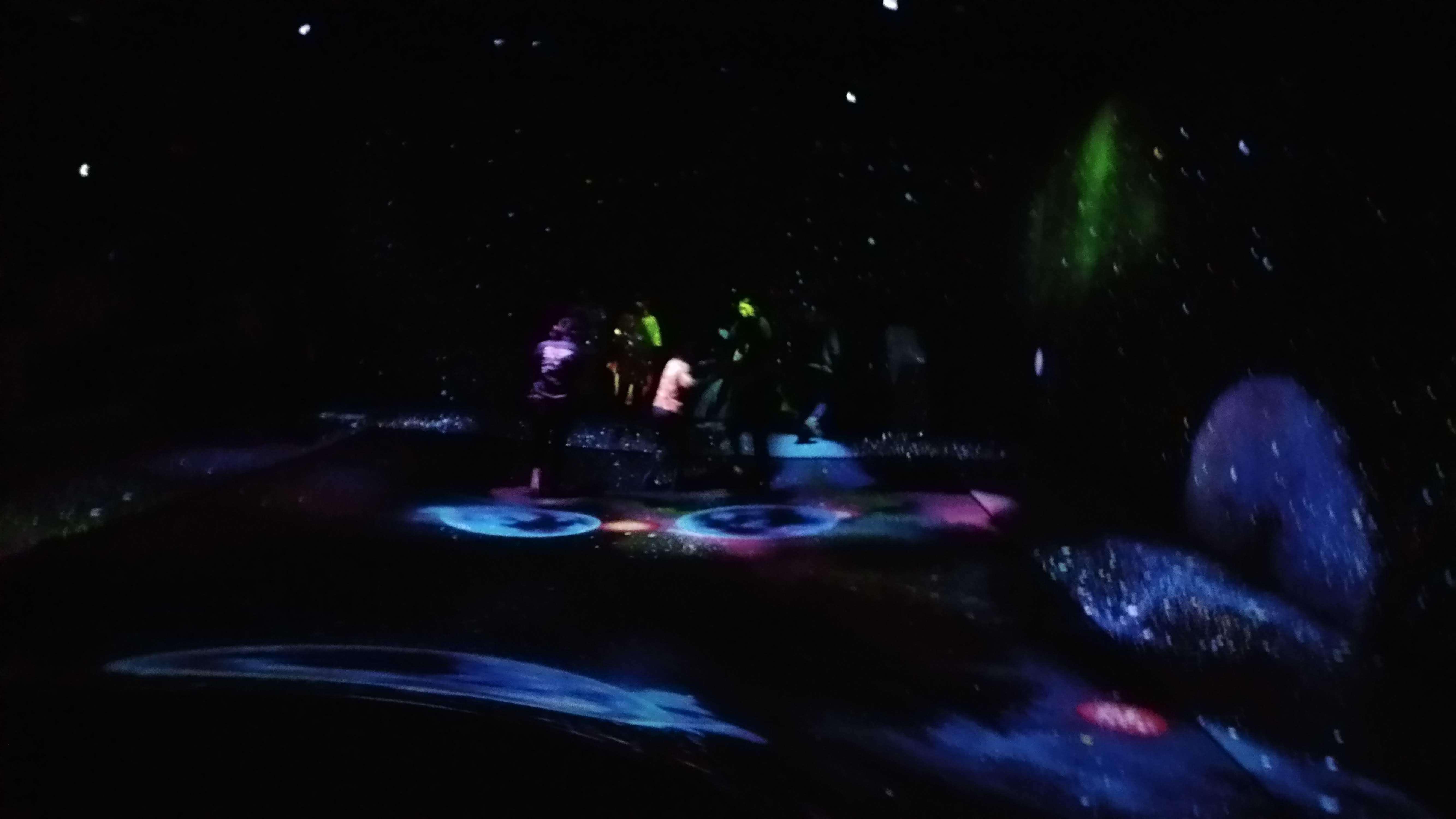 kids jump on a trampoline floor with planets projected on it