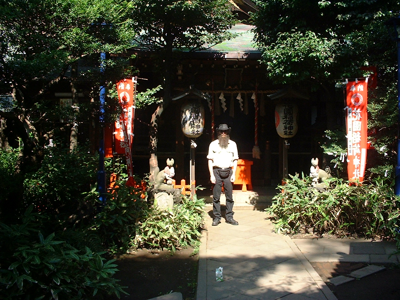 a bearded white man stands outside a small building obscured by trees